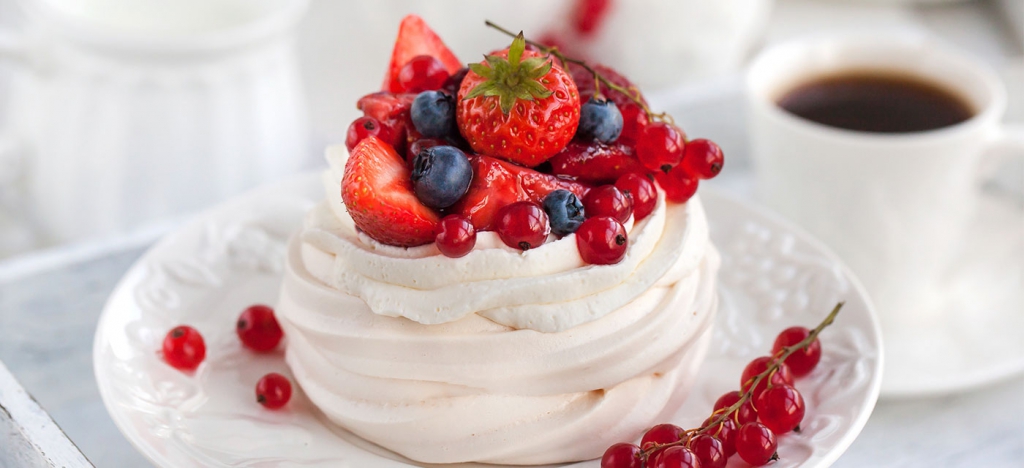 Pavlova (sobremesa de merengue assado) sobre um prato branco decorada com frutas vermelhas