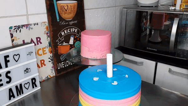 gif de um bolo rosa menor sendo disposto em cima de um bolo maior que é a base do bolo 